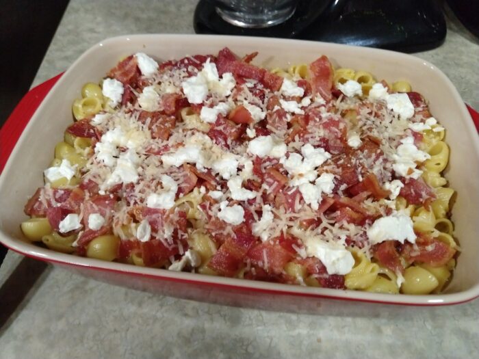 a casserole dish of macaroni and cheese topped with bacon and goat cheese