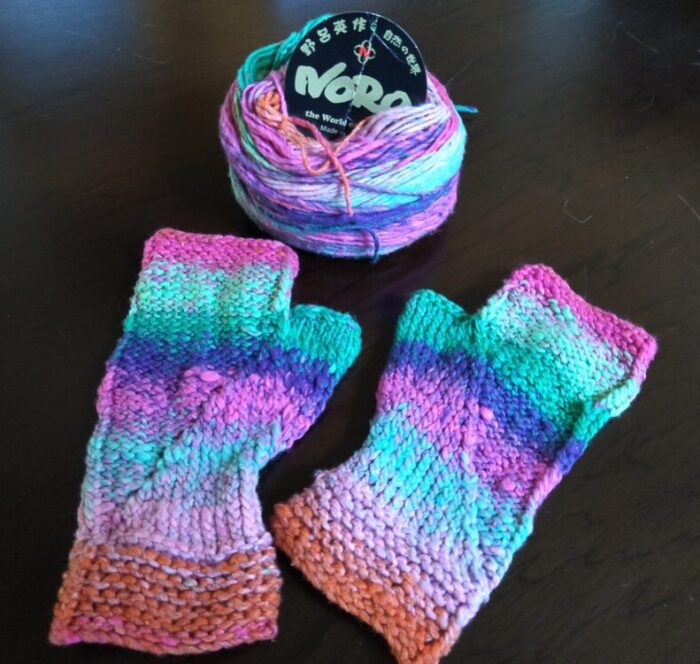 a pair of hand-knit fingerless gloves made in a yarn whose colorway moves from pink to blue, to purple to green