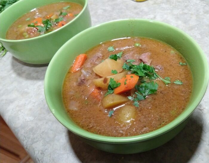 two bowls of beef stew containing carrots, potatoes, and beef, topped with parsley