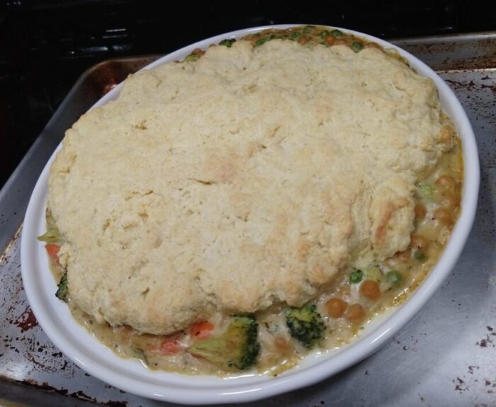 a pot pie topped in a biscuit crust. Chickpeas, broccoli, carrots, and peas are visible around the edges where the biscuit doesn't reach the border of the pie pan