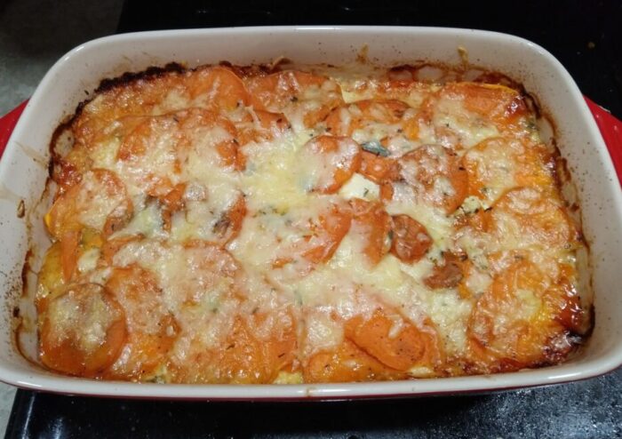 a casserole dish of sweet potato gratin. Sliced rounds of sweet potato topped with cheese and sage are visible