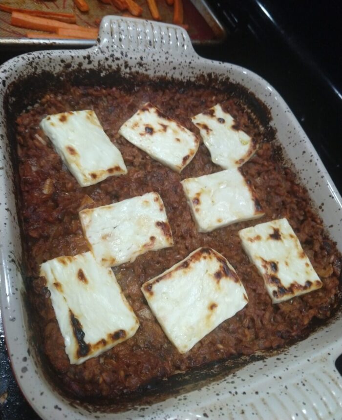 a casserole dish with baked farro and lentils in a tomato sauce, topped with slices of feta charred under the broiler