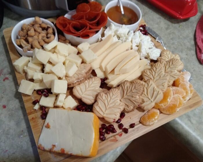a cheese board containing several types of cheese, cashews, honey, pepperoni, and maple leaf cookies