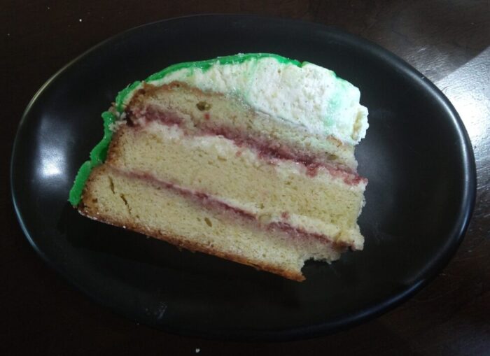 a slice of cake: three layers with pastry cream and jam in between each. The top has a dome of cream and green marizpan covers the entire outside.