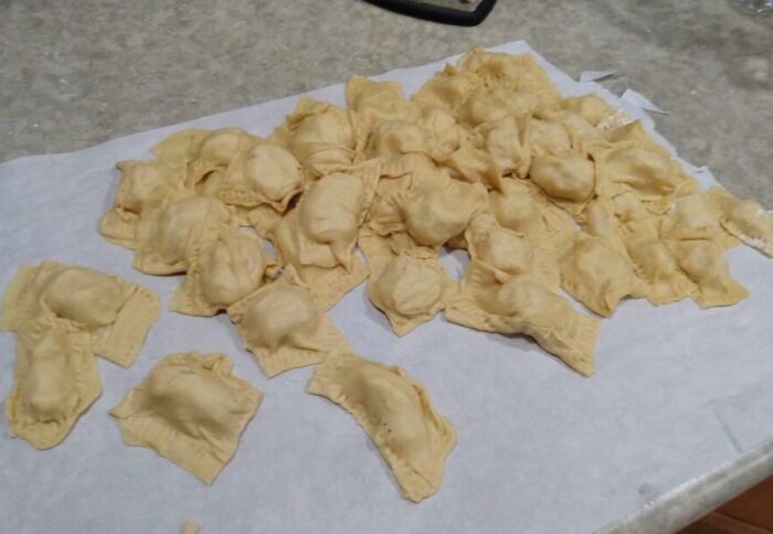 A pile of uncooked, handmade raviolis haphazardly stacked on a sheet of parchment paper.