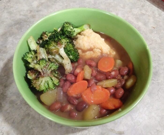 a bowl with polenta topped with a mix of beans, potatoes, and carrots along with some roasted broccoli