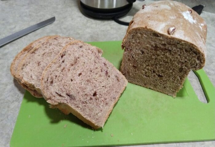 A loaf of bread, with half the loaf cut into slices. It's a medium-brown color from wheat flour and studded with pecans.