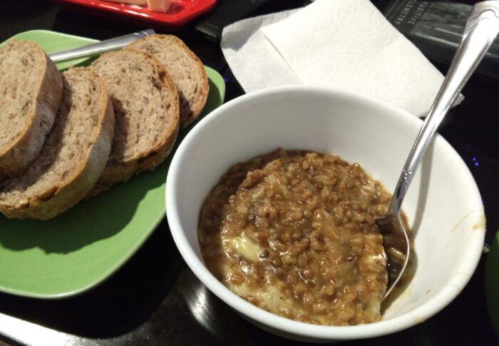 a bowl of lentils and farro cooked with caramelized onions and topped with cheese. A plate of sliced bread is to the side.