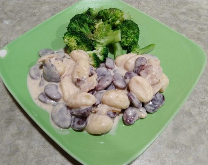 a plate with a pile of beans and gnocchi in gorgonzola sauce plus some broccoli