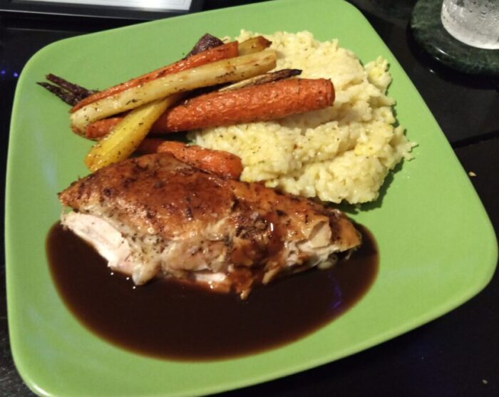 a plate of chicken breast with gravy, roast carrots, and risotto