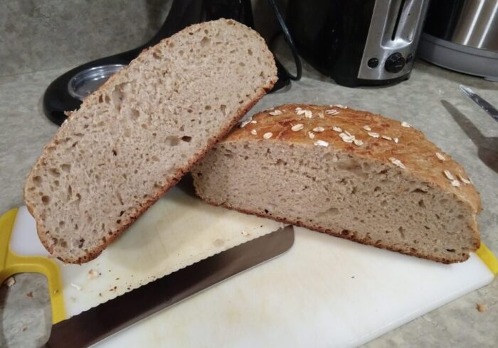 a loaf of no-knead oat bread, cut in half to reveal a somewhat under-proofed middle
