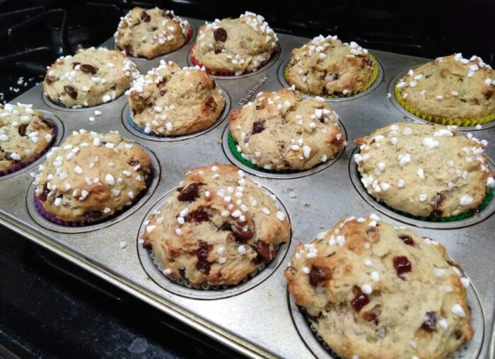 12 muffins fresh from the oven, still in the pan. They are studded with chocolate chips and jammy bits and topped with pearl sugar