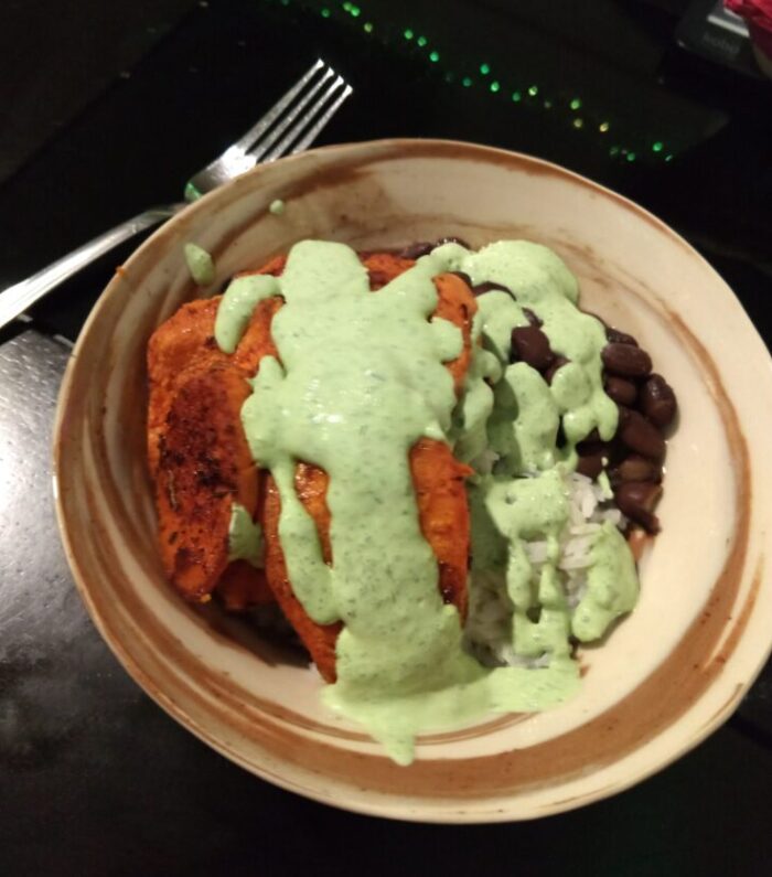 a bowl of rice topped with beans, roasted sweet potato, and a green sour cream sauce