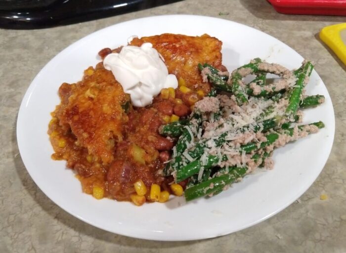 a plate of vegetarian tamale pie with a dollop of sour cream and a pile of green beans in walnut sauce