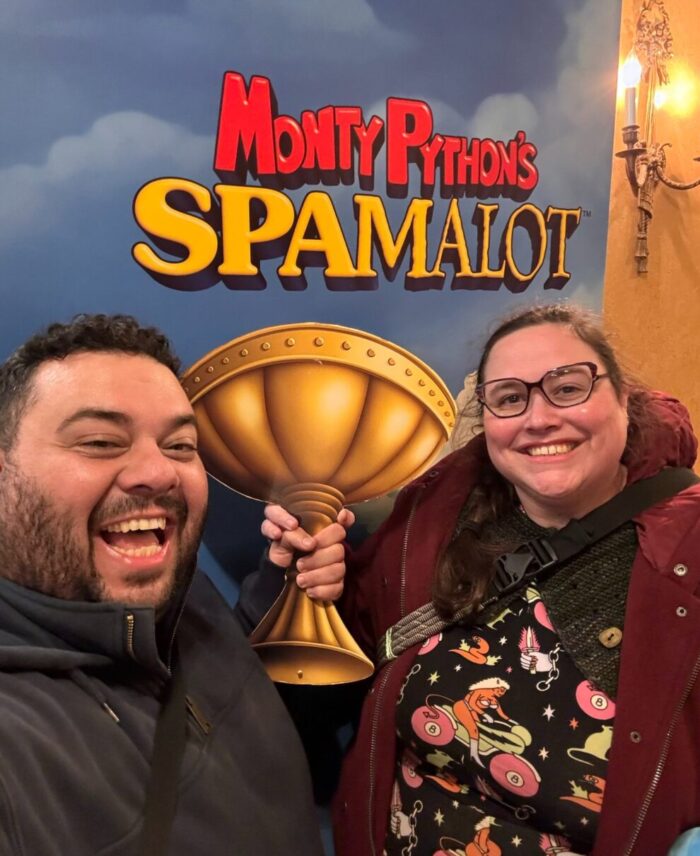 Lito and I holding a holy grail cutout and grinning in front of a "Monty Python's Spamalot" backdrop