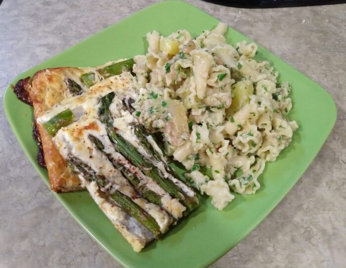 A plate of pasta mixed with beans, potato, and a pesto-like sauce. There are also pieces of asparagus tart