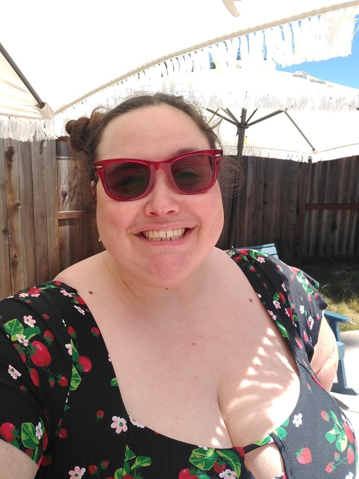 Me, outside, wearing red sunglasses and a cute swimsuit, smiling at the camera. My hair is in two buns on top of my head