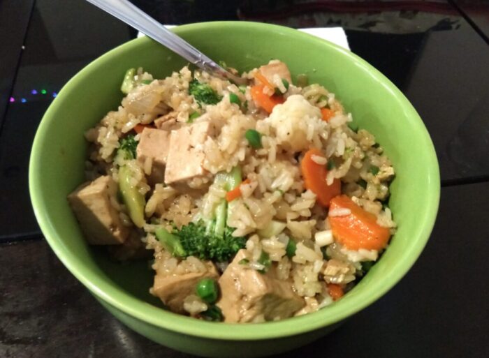 a bowl of tofu and broccoli fried rice, also included are carrots and peas