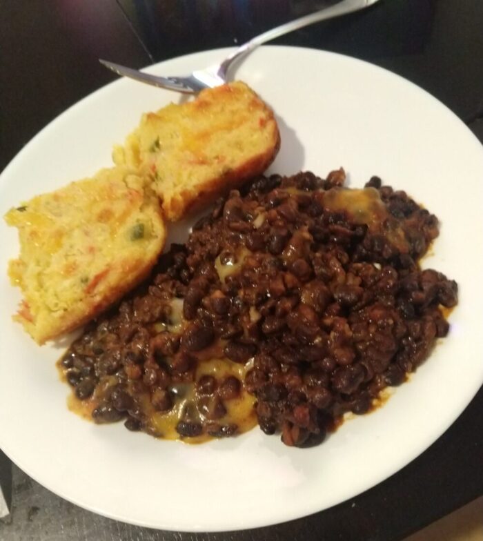 a plate of black beans with melty cheese and two corner pieces of southwestern corn spoonbread