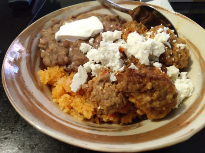 a bowl full of albóndigas, beans, and rice, topped with queso fresco