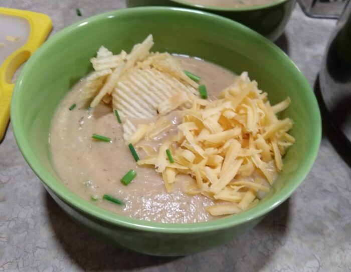 a bowl of potato, cauliflower and bean soup topped with potato chips, cheese, and chives