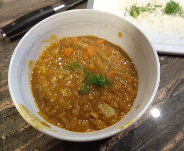 A bowl of soup topped with fennel bits. Chunks of fennel and carrot are visible along with the farro
