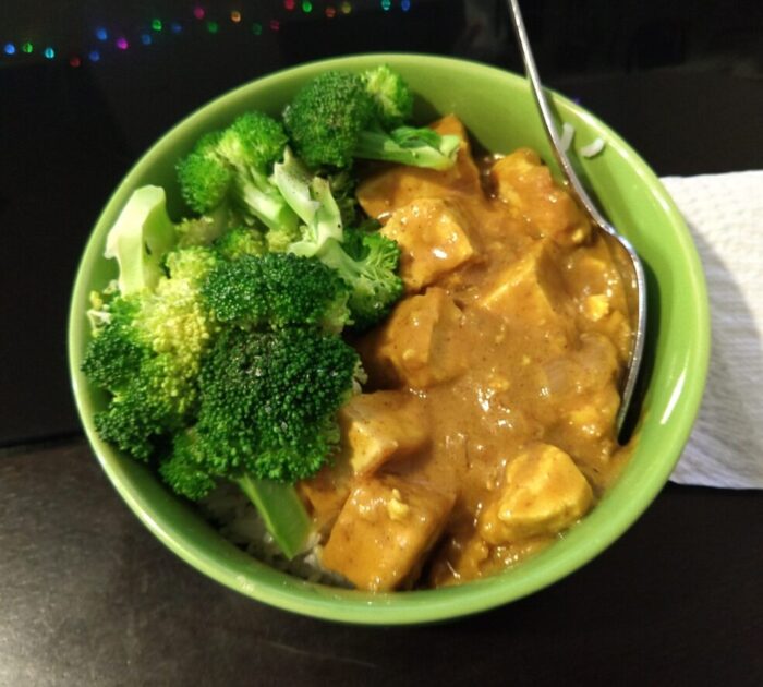 A bowl of tofu in peanut sauce and some broccoli on top of rice