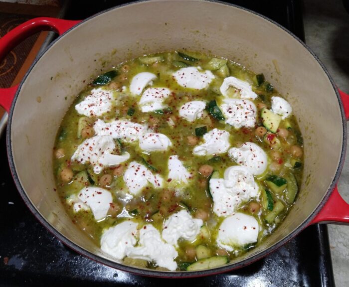 big pot full of braised chickpeas with zucchini and pesto topped with chunks of burrata