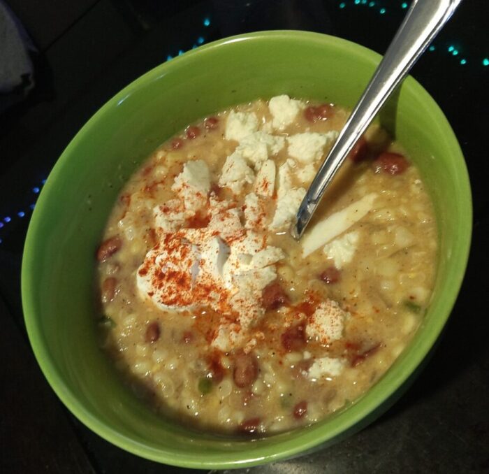 a bowl of corn and bean chowder topped with cotija cheese and sour cream