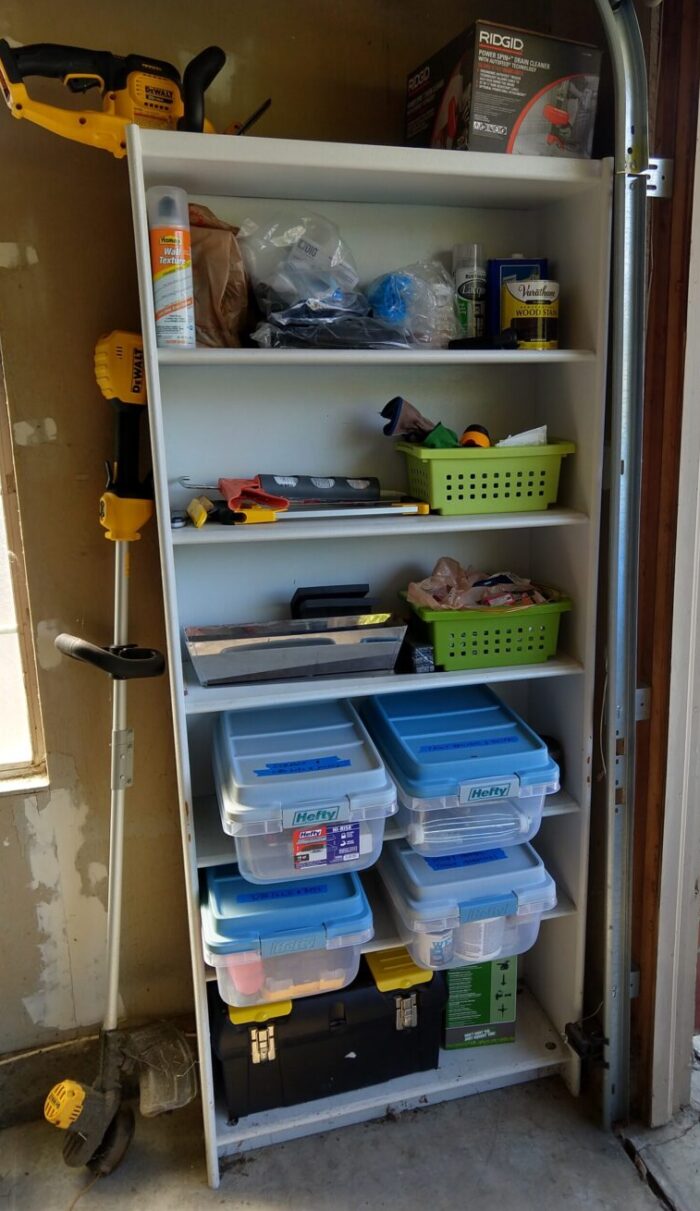 A bookcase in my garage with newly cleaned shelves, some things in neat piles, and some small plastic bins on some shelves