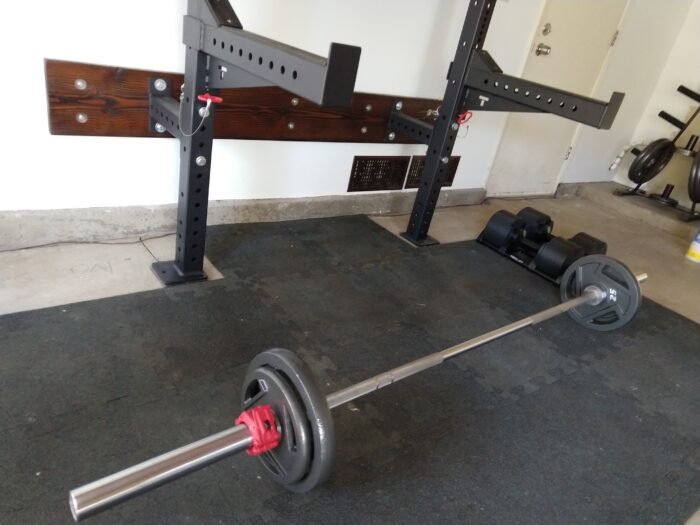 a bar with 25 and 10 pound weights on it, on the ground in front of a squat rack