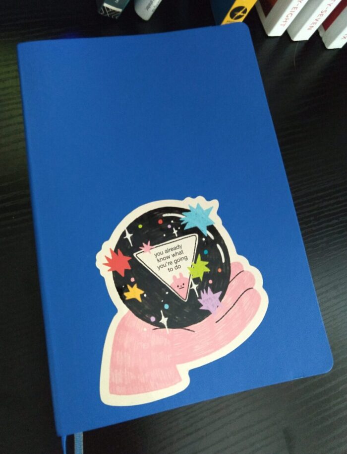 A bright-blue planner with a sticker of a magic 8 ball that says "you already know what you're going to do" inside