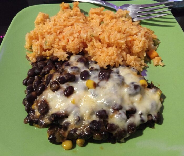 a plate black beans with corn topped with melted cheese, and a pile of rice