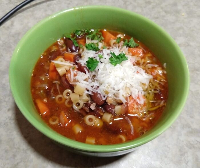 A bowl of pasta and bean soup topped with grated parmesan and bits of parsley