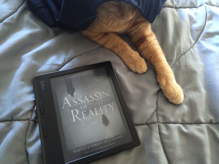 book cover for Assassin of Reality shown on kobo ereader. Fritz the cat has his head covered by his pants and his paws stretched out near the book