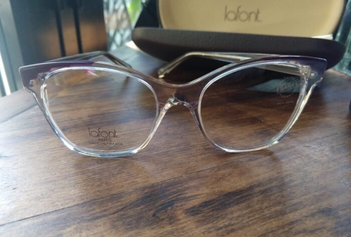 a pair of clear, cat-eye shaped glasses frames with purple accents on the top corners.