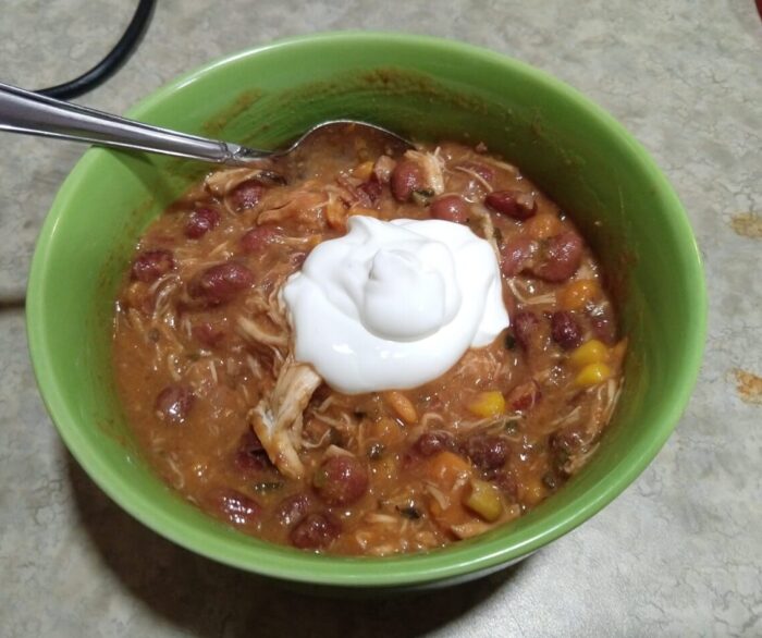 a bowl of chili containing beans, sweet potatoes, corn, and chicken, and topped with sour cream