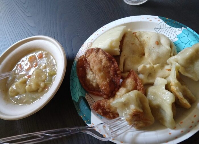 a paper plate with an assortment of dumplings next to a small bowl with chicken and dumplings