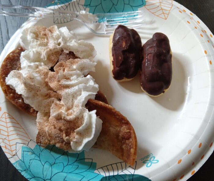 a paper plate with pumpkin pie dumplings covered in whipped cream, and chocolate eclairs