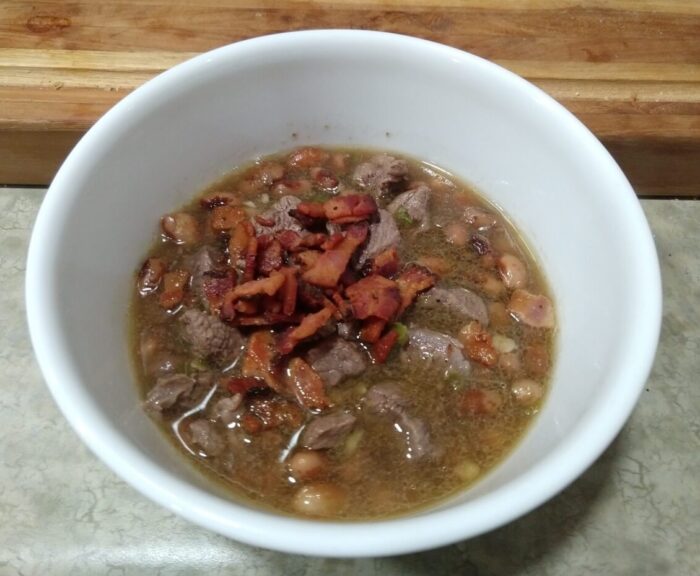 a bowl of carne en su jugo (beans topped with stewed, brothy beef and crispy bacon)