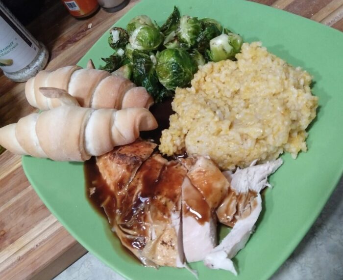 a plate of roast chicken, butternut squash risotto, brussels sprouts, and crescent rolls