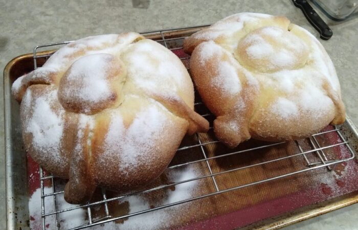 Two round loaves of pan de muerto topped with sugar, cooling on a wire rack