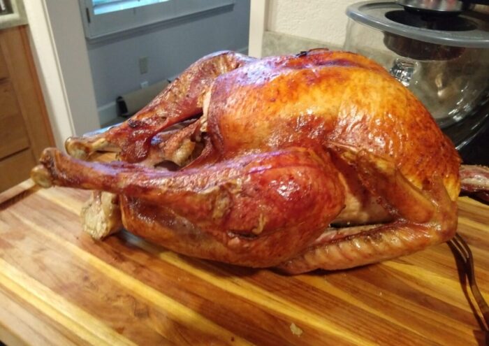 a big roasted turkey, nicely bronzed, sitting on a cutting board waiting to be carved