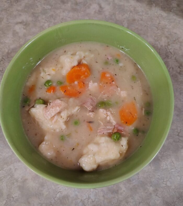 a bowl of turkey and dumplings with bits of carrot and peas visible in the broth