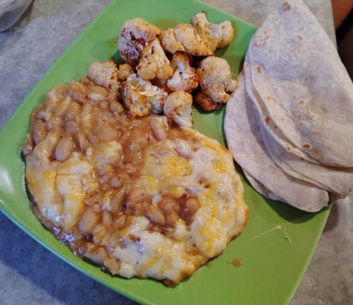 a plate of cheesy beans, roasted cauliflower, and tortillas