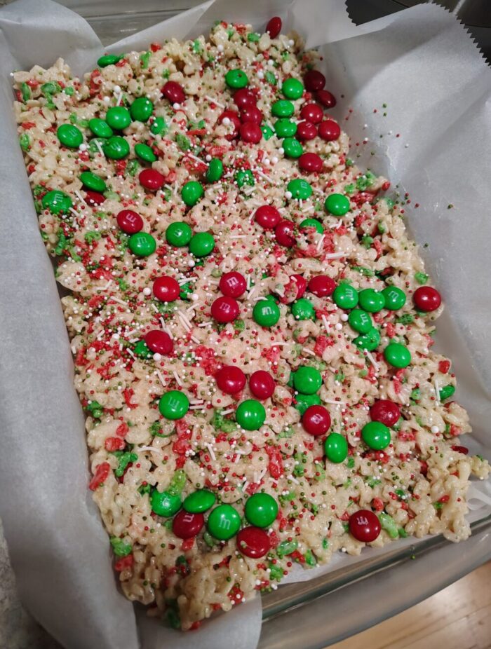 a pan of rice krispie treats made with christmas-colored cereal and topped with red and green m&ms and sprinkles