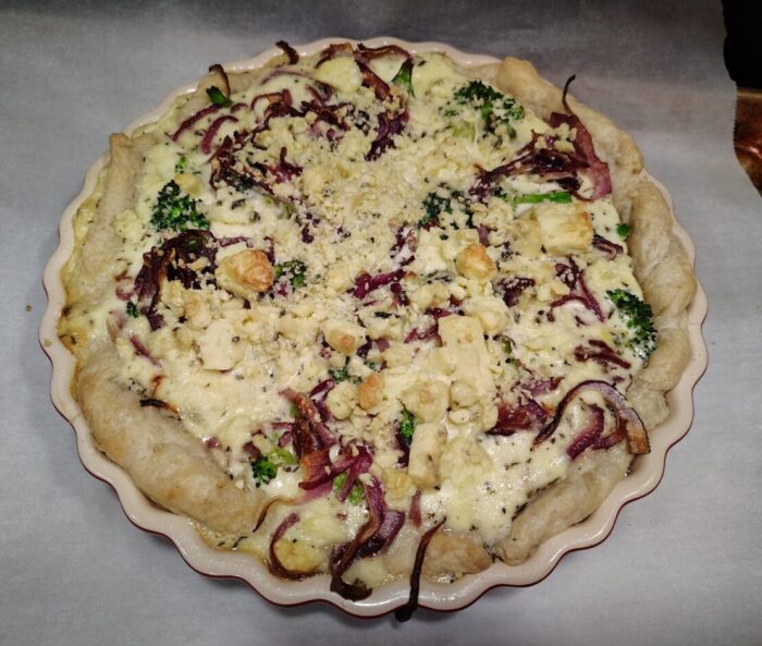 A broccoli, onion, and blue cheese tart. Strands of red onion and broccoli florets are visible through the custard