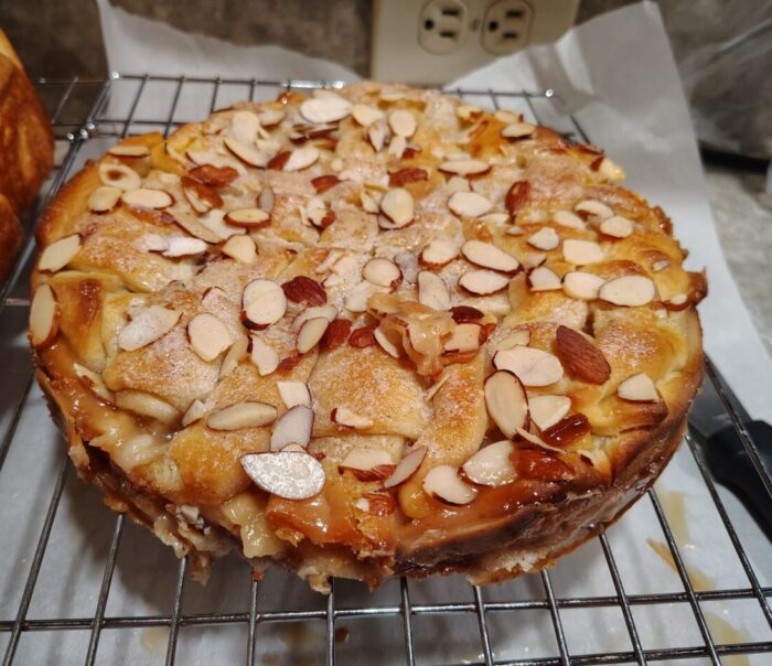 A round cake with a lattice top that is covered with sugar and slivered almonds. The cake's sugary filling has caramelized around the edges.