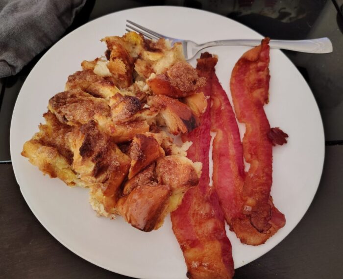 a big chunk of french toast casserole and several slices of bacon on a plate