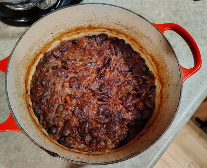 A dutch oven of Serbian baked beans, baked down so the beans and onions on top are caramelized and there is barely any broth remaining